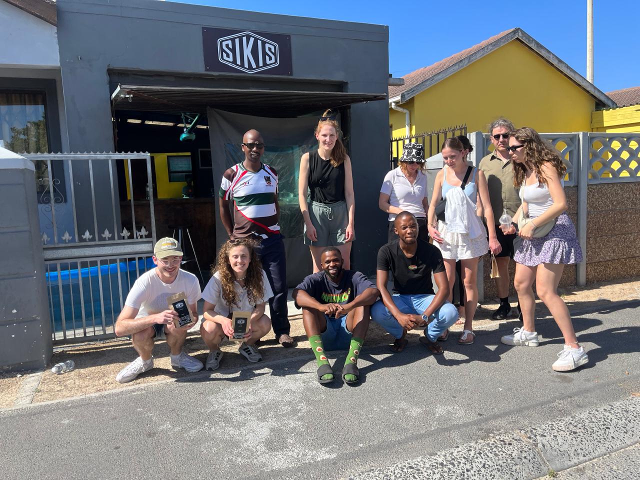 Tour group posing with a local host outside a township shop