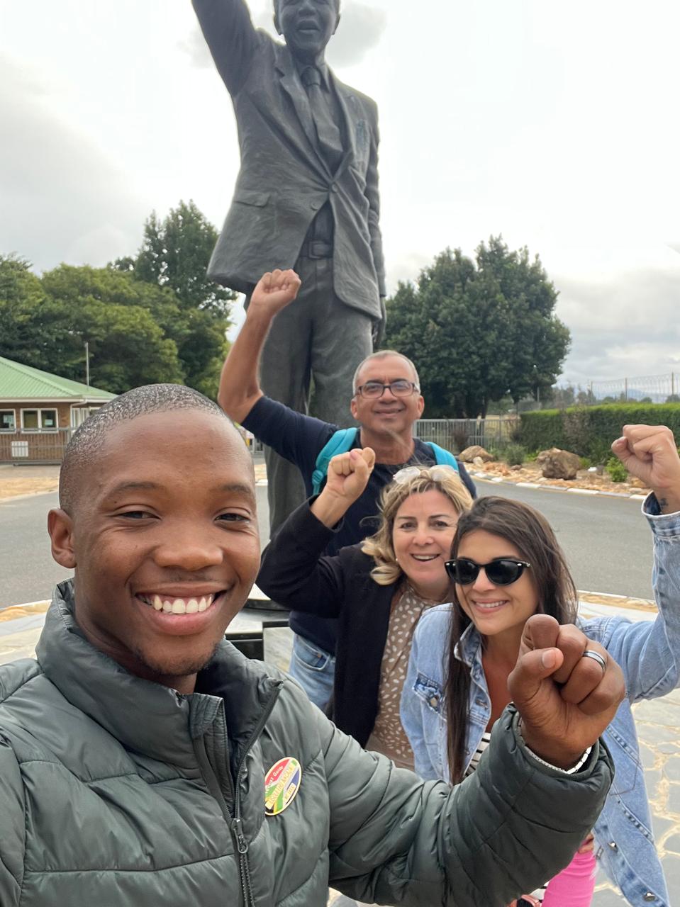 Guide and guests raising fists at a Nelson Mandela statue