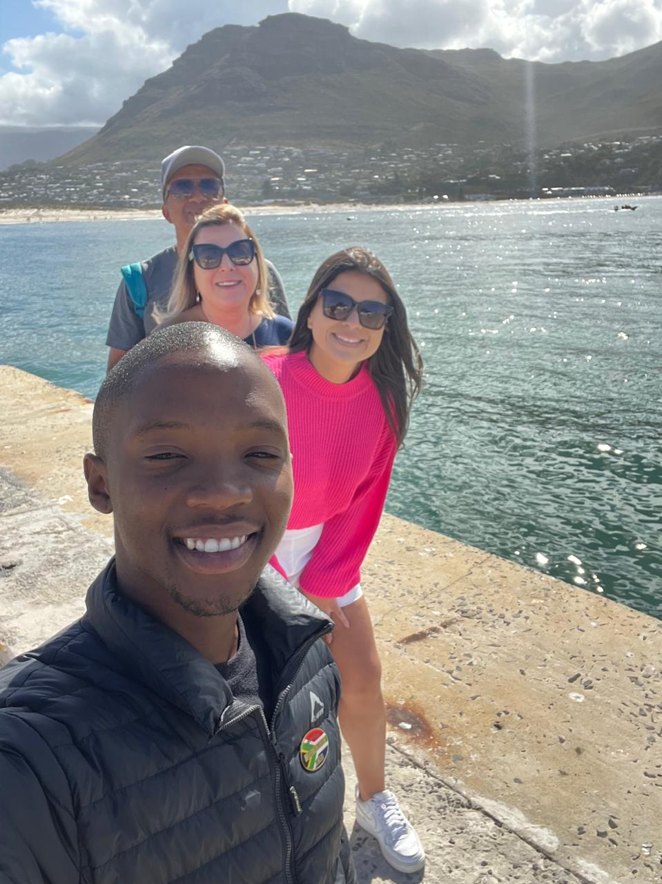 Guide and guests at Hout Bay harbour with Chapman's Peak behind